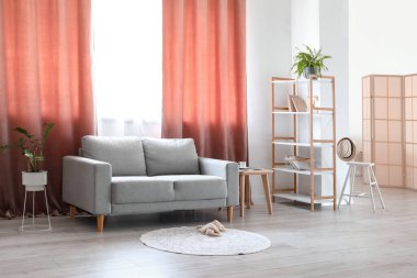 Gri kanepe, raf ünitesi ve kırmızı perdelerle aydınlık oturma odasının içinde.