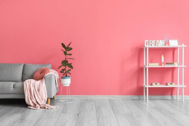 Oturma odasının içinde rahat bir kanepe ve pembe duvarın yanında raflar.