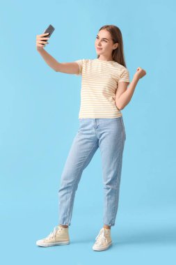 Cep telefonlu güzel bir kadın mavi arka planda selfie çekiyor.