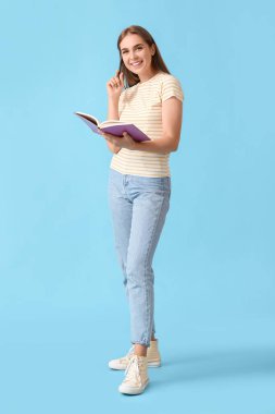 Mavi arka planda kalem ve açık not defteri olan güzel bir genç kadın.