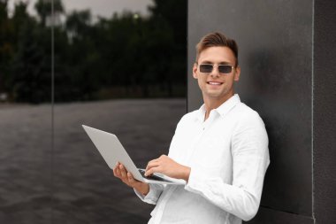 Dışarıda dizüstü bilgisayar kullanan güneş gözlüklü yakışıklı bir genç.