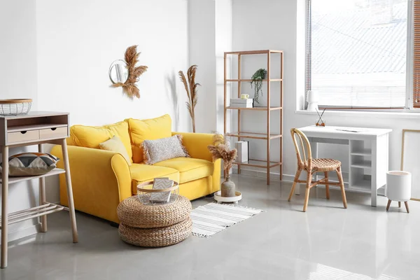 Interior of stylish living room with yellow sofa, workplace and dry reeds