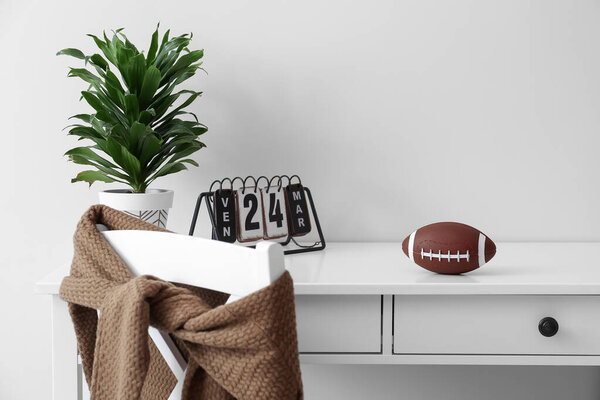 Rugby ball with calendar and houseplant on table near white wall