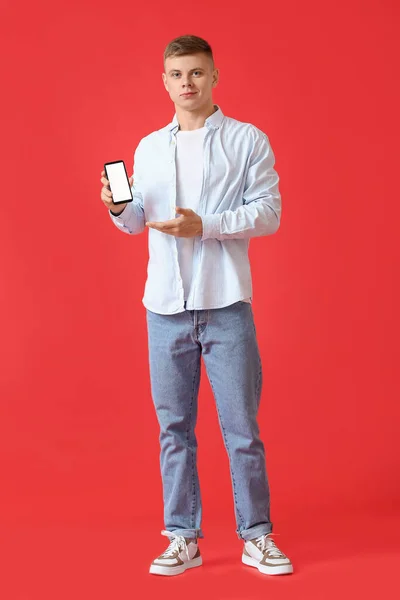 Jóképű Fiatalember Mutatja Mobiltelefon Piros Háttér — Stock Fotó