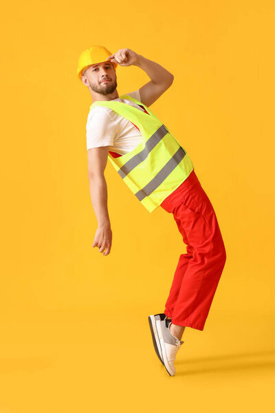 Young male worker dancing on yellow background