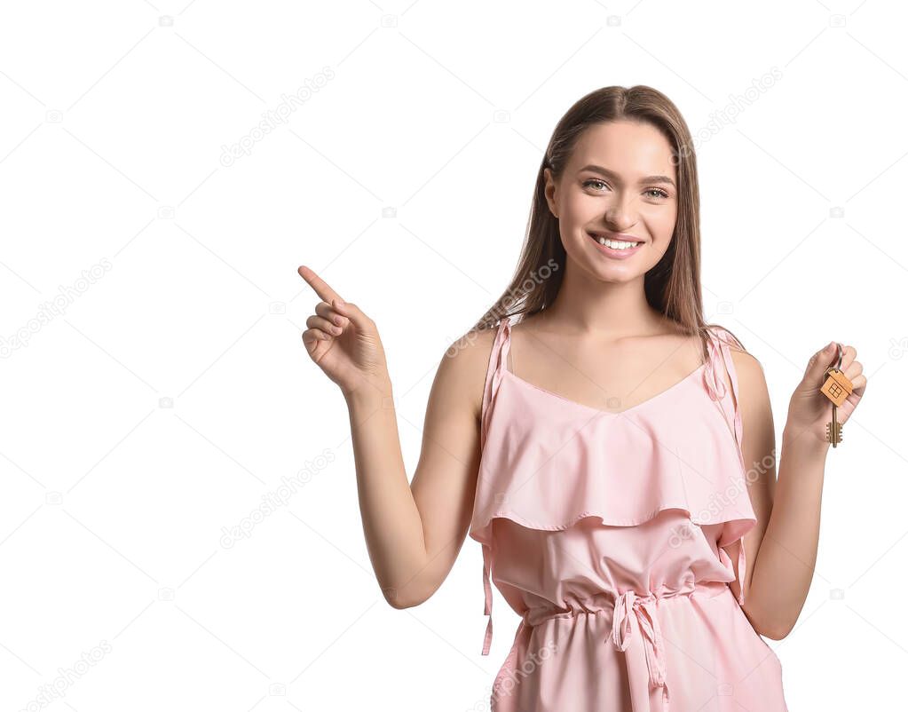 Smiling young woman with key from house pointing at something on white background