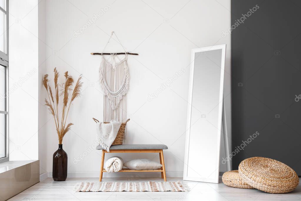 Soft bench with basket, plaid, pillow and dry reeds in vase near light wall
