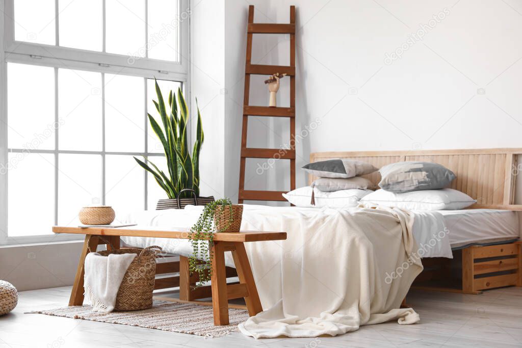 Wooden bench with basket and houseplant in interior of light bedroom
