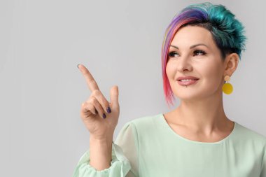 Gri arkaplandaki bir şeyi gösteren tuhaf saçlı güzel bir kadın.