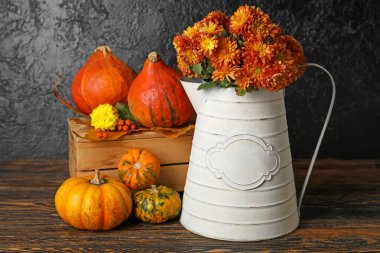 Kasımpatı çiçekleri ve balkabaklarıyla sulanan teneke kutu siyah arka planda.