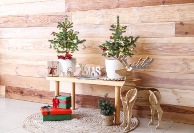 Küçük Noel ağaçları, hediyeler ve ahşap duvarın yanında ren geyiği olan bir bank.