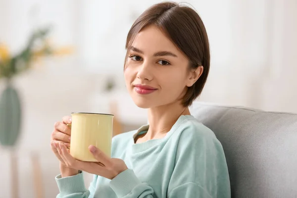 漂亮的年轻女子在家里沙发上喝着美味的茶 — 图库照片