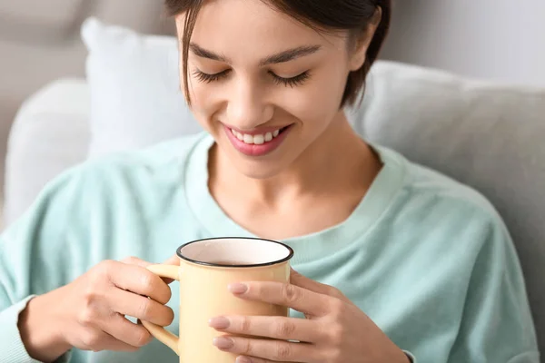 漂亮的年轻女子在家里沙发上喝着美味的茶 — 图库照片