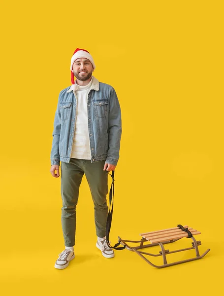 サンタ ハットの若い男とそりの色の背景 — ストック写真