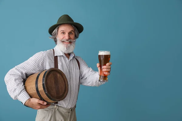 Handsome senior man in traditional German clothes and with beer on color background