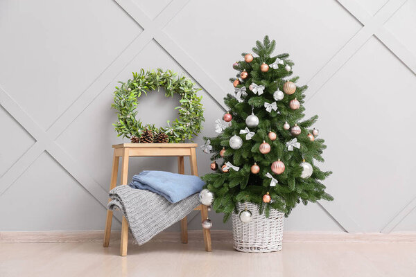 Beautiful Christmas tree and table with wreath near light wall