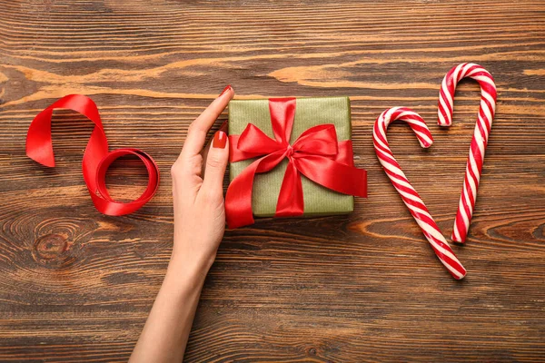 Mão Feminina Com Presente Natal Bengalas Doces Fita Fundo Madeira — Fotografia de Stock