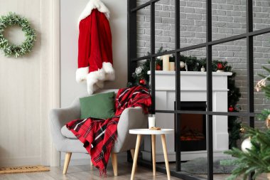 Bir bardak süt, koltuğun yanındaki masada kurabiyeler ve Noel Baba kostümü. Kapıda Noel çelengi asılı.