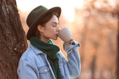 Güneşli bir sonbahar gününde parkta çay içen güzel bir kadın.