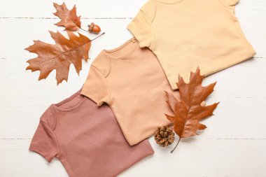 Hafif ahşap arka planda bebek kıyafetleri ve sonbahar yaprakları.