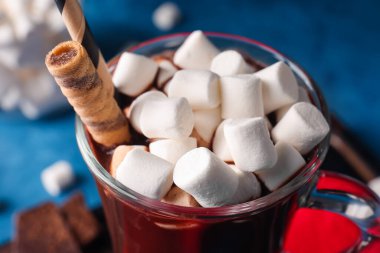 Mavi arka planda lokum bulunan bir bardak lezzetli sıcak çikolata, yakın plan.