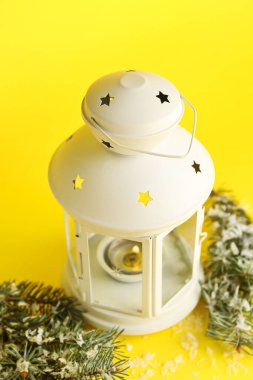 Sarı arka planda yanan mum ve köknar dallarıyla güzel bir Noel feneri.