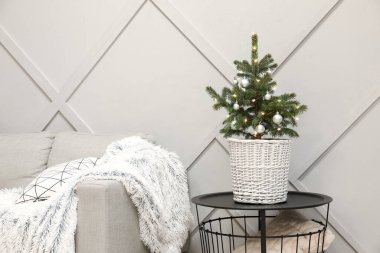 Masadaki saksıda güzel süslenmiş Noel ağacı ve ışık duvarının yanındaki rahat kanepe.