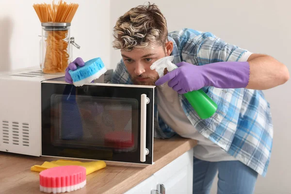 Jovem Bonito Com Esponja Limpeza Microondas Cozinha — Fotografia de Stock