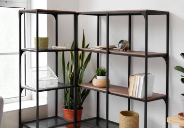 Kitapları ve ışık duvarının yanında bitkileri olan siyah raf ünitesi.