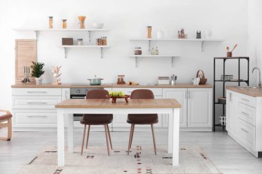 Mutfağın içinde yemek masası, yiyecek ve raflar var.