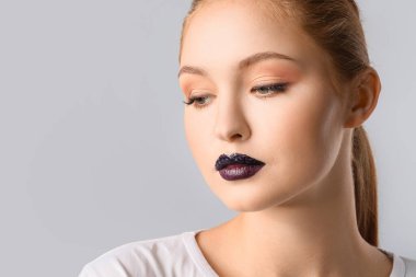 Gri arka planda olağandışı makyajı olan güzel bir genç kadın.