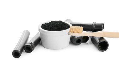 Aktif kömür diş tozu, bambu çubukları ve beyaz arka planda fırça ile kase