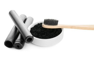 Aktif kömür diş tozu, bambu çubukları ve beyaz arka planda fırça ile kase