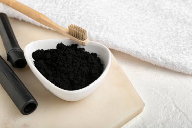 Beyaz arka planda aktif kömür diş tozu, fırça ve bambu çubukları ile kase