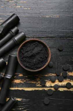 Aktif hale getirilmiş kömür diş tozu, haplar ve siyah ahşap arka planda bambu çubukları olan kase.