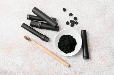 Işık arka planında aktif kömür diş tozu, fırça ve bambu çubukları olan kase