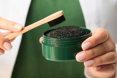 Kavanoz tutan kadın aktif kömür diş tozu ve fırça, yakın plan.