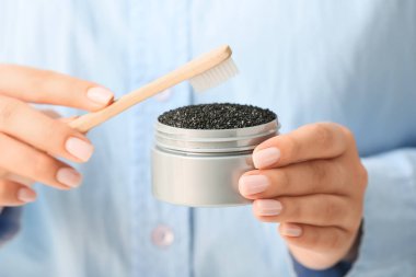 Kavanoz tutan kadın aktif kömür diş tozu ve fırça, yakın plan.