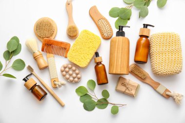 Beyaz arka planda süngerli, fırçalı ve bitki dallı banyo malzemeleri.