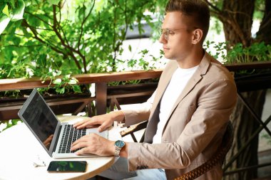 Caddedeki kafede dizüstü bilgisayar kullanan yakışıklı bir genç.