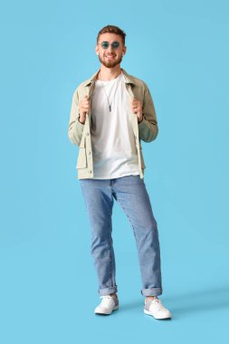 Mavi arka planda ceketli şık bir genç.
