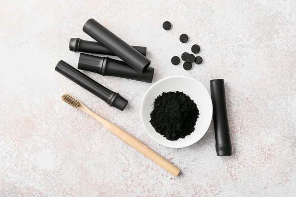Bowl with activated charcoal tooth powder, brush and bamboo sticks on light background