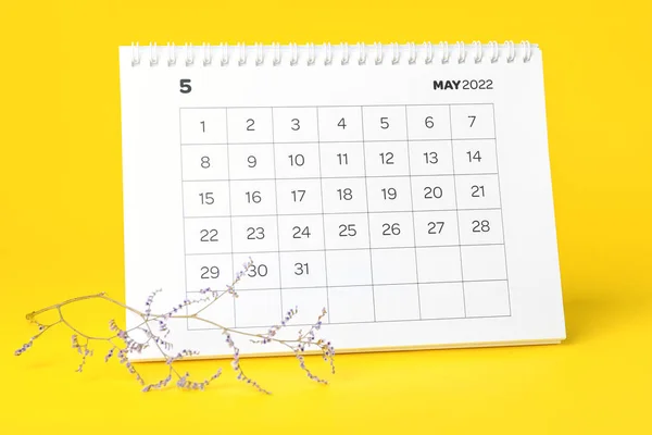 2022年5月的折页日历和黄色背景的花枝 — 图库照片