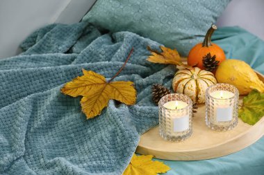 Tutacaklarda mum yakmak ve kanepede sonbahar dekorasyonu yapmak.