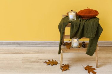 Sarı duvarın yanındaki merdivende yanan mumlar, süveter ve sonbahar dekoru.