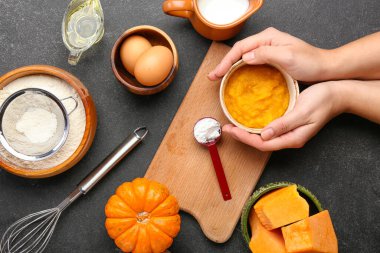 Siyah arka planda balkabağı turtası hazırlamak için malzemeli kadın elleri.