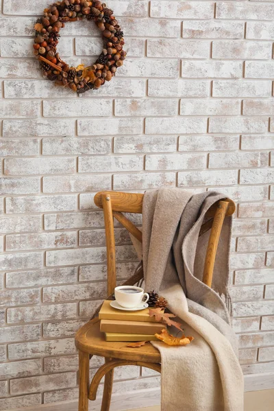 明るいレンガの壁に美しいアコーンの花輪と部屋の椅子に本とコーヒーカップ — ストック写真