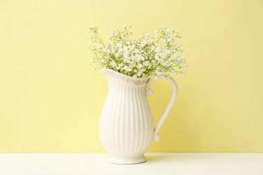 Renkli duvarın yanındaki masada güzel çingene çiçekleri olan bir sürahi.