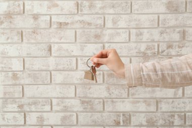 Tuğla arka planda ev anahtarı olan bir emlakçı.