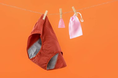 Adet külotu, regl kupası ve renkli arka planda asılı duran bir çanta.